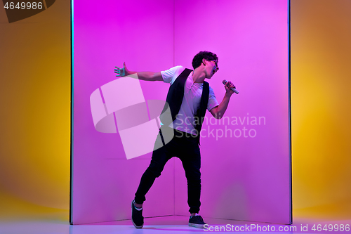 Image of Young male musician, singer performing on pink-orange background in neon light