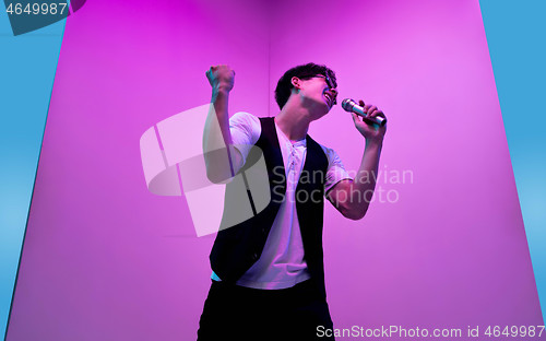 Image of Young male musician, singer performing on pink-blue background in neon light