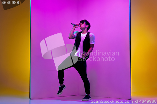 Image of Young male musician, singer performing on pink-orange background in neon light