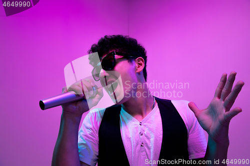 Image of Young male musician, singer performing on pink background in neon light