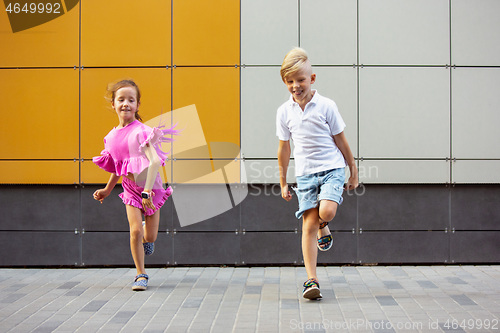 Image of Two smiling kids, boy and girl running together in town, city in summer day