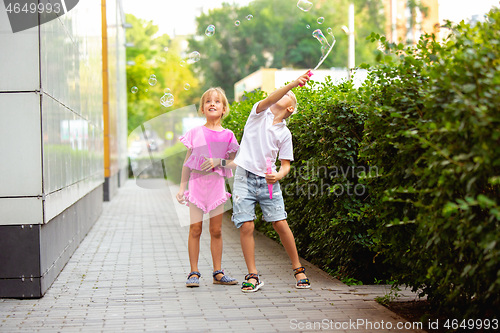 Image of Two smiling kids, boy and girl running together in town, city in summer day