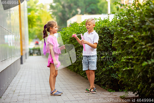 Image of Two smiling kids, boy and girl running together in town, city in summer day