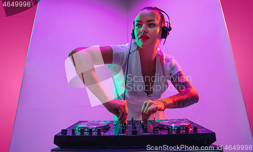 Image of Young caucasian female musician in headphones performing on purple background in neon light