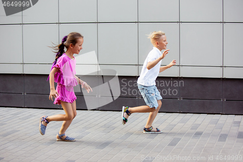 Image of Two smiling kids, boy and girl running together in town, city in summer day