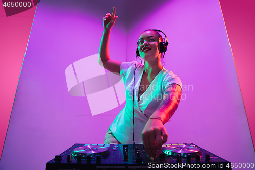 Image of Young caucasian female musician in headphones performing on purple background in neon light