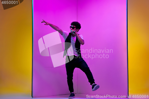 Image of Young male musician, singer performing on pink-orange background in neon light