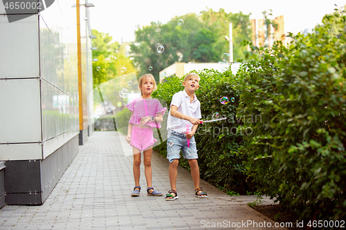 Image of Two smiling kids, boy and girl running together in town, city in summer day