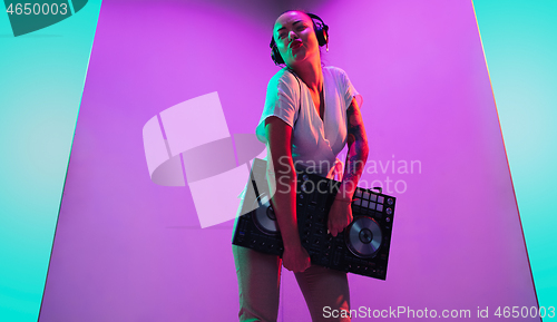 Image of Young caucasian female musician in headphones performing on purple background in neon light