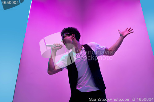 Image of Young male musician, singer performing on pink-bluebackground in neon light