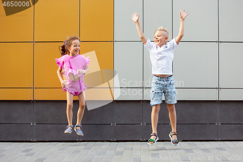 Image of Two smiling kids, boy and girl running together in town, city in summer day