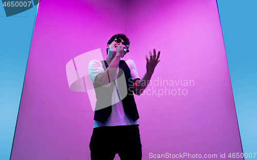 Image of Young male musician, singer performing on pink-bluebackground in neon light