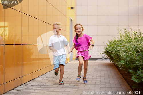 Image of Two smiling kids, boy and girl running together in town, city in summer day