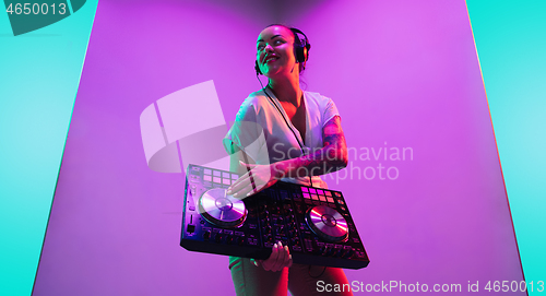 Image of Young caucasian female musician in headphones performing on purple background in neon light