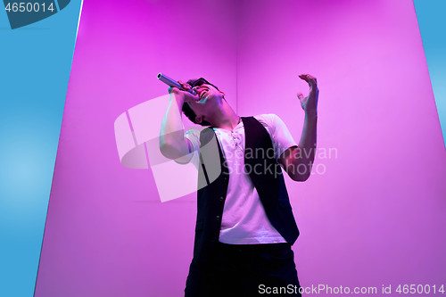 Image of Young male musician, singer performing on pink-bluebackground in neon light