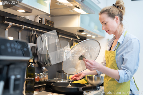 Image of Stay at home housewife woman cooking in kitchen, stir frying dish in a saucepan, preparing food for family dinner.