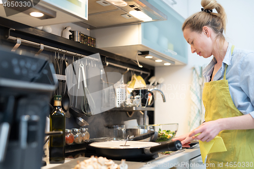 Image of Stay at home housewife woman cooking in kitchen, stir frying dish in a saucepan, preparing food for family dinner.