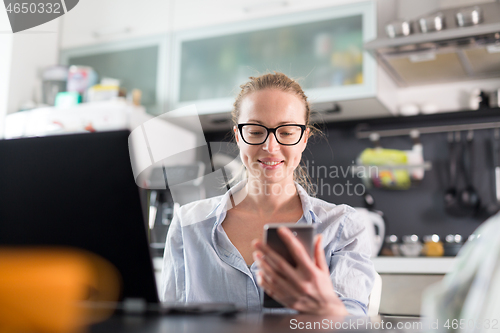 Image of Stay at home and social distancing. Woman in her casual home clothing working remotly from her kitchen dining table in the morning. Video chatting with friend, family or business clients or partners