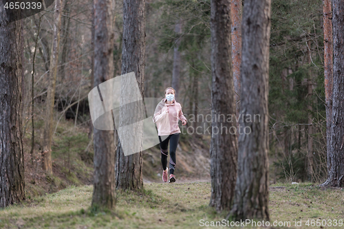 Image of Corona virus, or Covid-19, is spreading all over the world. Portrait of caucasian sporty woman wearing a medical protection face mask while running in nature.