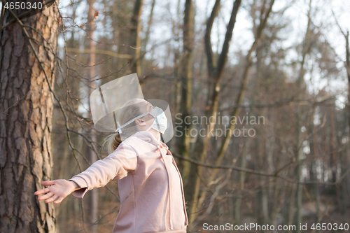 Image of Portrait of caucasian sporty woman wearing medical protection face mask while relaxing by taking a deep breath in forest. Corona virus, or Covid-19, is spreading all over the world