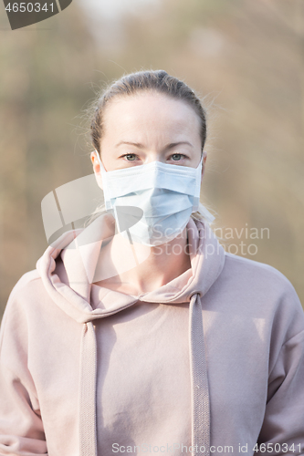 Image of Portrait of caucasian sporty woman wearing medical protection face mask while walking in park, relaxing and listening to music. Corona virus, or Covid-19, is spreading all over the world