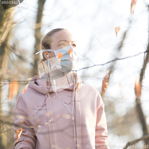 Image of Portrait of caucasian sporty woman wearing medical protection face mask while walking in park, relaxing and listening to music. Corona virus, or Covid-19, is spreading all over the world