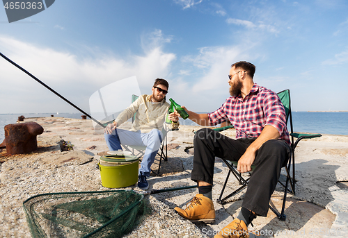 Image of male friends fishing and drinking beer on sea pier