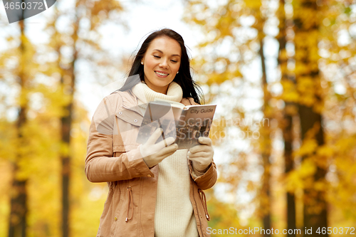 Image of happy young woman with city guide in autumn park