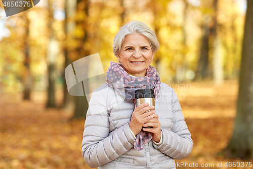 Image of old woman with hot drink in tumbler at autumn park