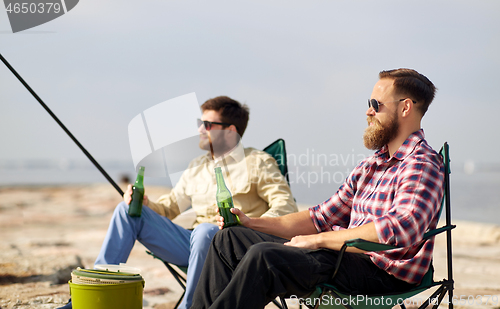 Image of happy friends fishing and drinking beer on pier