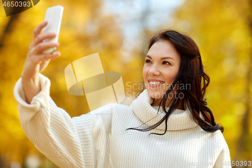 Image of woman taking selfie by smartphone at autumn park