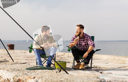 Image of happy friends fishing and eating sandwiches