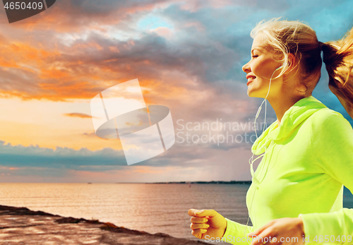Image of woman with earphones running over sea sunset