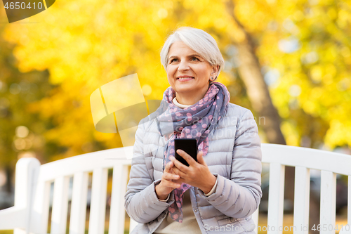 Image of happy senior woman with smartphone at autumn park