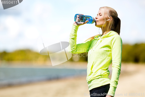 Image of woman drinking water after exercising on beach