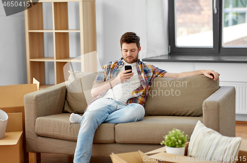 Image of man with smartphone and boxes on sofa at new home