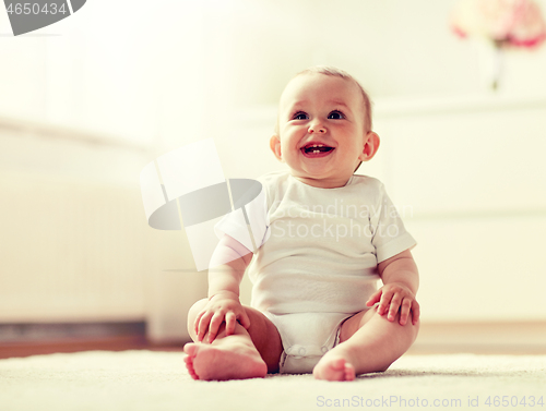 Image of happy baby boy or girl sitting on floor at home