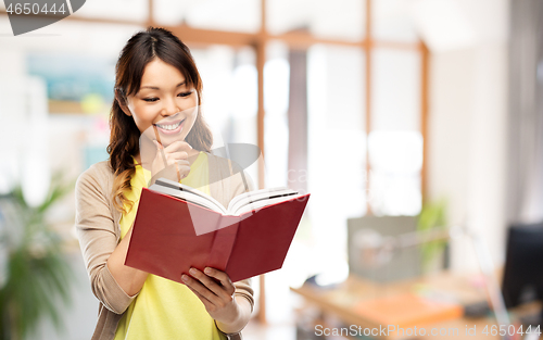 Image of happy asian woman reading book at office