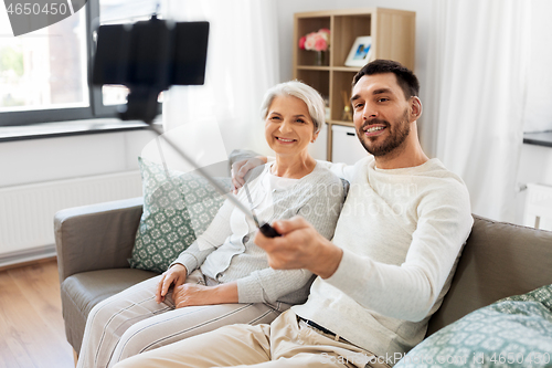 Image of senior mother with adult son taking selfie at home