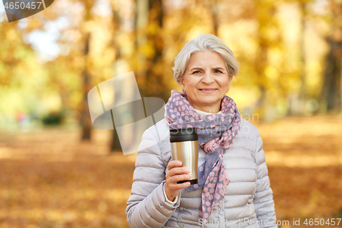 Image of old woman with hot drink in tumbler at autumn park