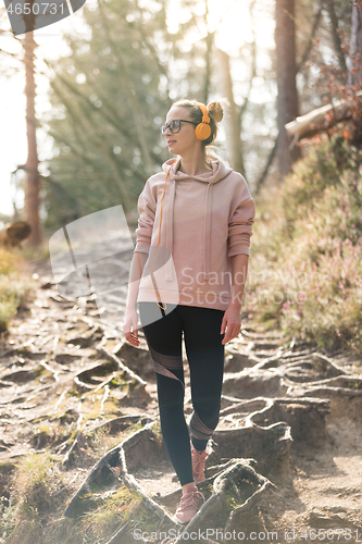 Image of Active sporty woman listening to the music while hiking in autumn fall forest. Female jogger training outdoor. Healthy lifestyle image of young caucasian woman walking on hiking trail in nature