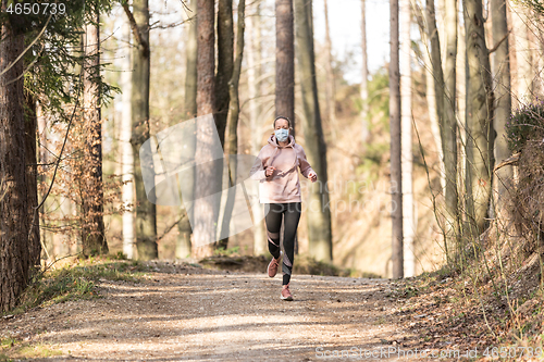 Image of Corona virus, or Covid-19, is spreading all over the world. Portrait of caucasian sporty woman wearing a medical protection face mask while running in nature.