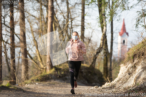 Image of Corona virus, or Covid-19, is spreading all over the world. Portrait of caucasian sporty woman wearing a medical protection face mask while running in nature.