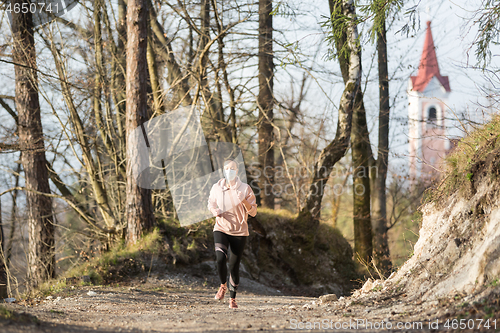 Image of Corona virus, or Covid-19, is spreading all over the world. Portrait of caucasian sporty woman wearing a medical protection face mask while running in nature.