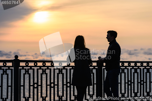 Image of Two young people are talking while standing at sunset against the backdrop of the sea landscape