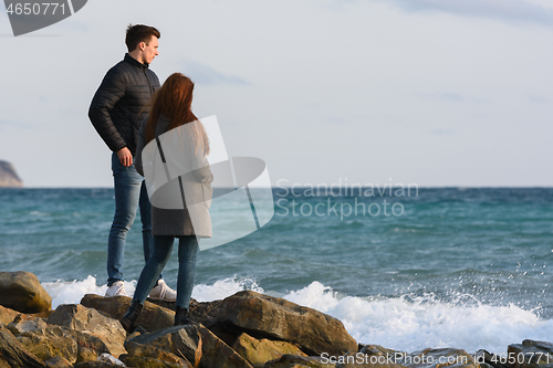 Image of Two young people standing on a stone beach discussing the current situation.