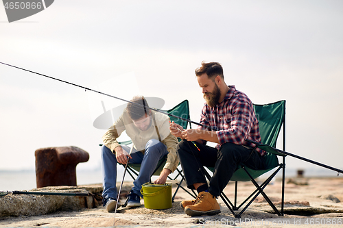 Image of friends adjusting fishing rods with bait on pier