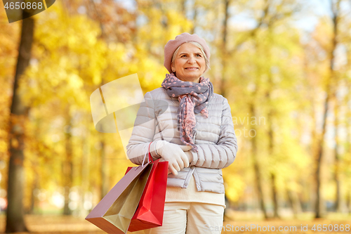 Image of senior woman with shopping bags at autumn park