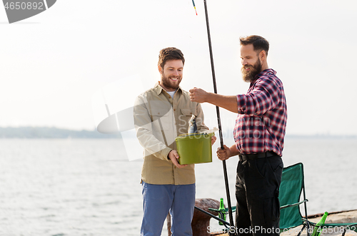 Image of male friends with fish and fishing rods on pier