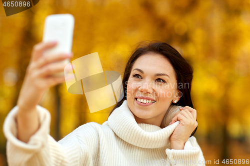 Image of woman taking selfie by smartphone at autumn park